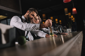 Wall Mural - male bartender showing colleague how to prepare drink at bar