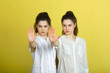 © Alexandr - two beautiful young girl sisters twins in white blouses on a yellow background with serious faces and gesture of hands