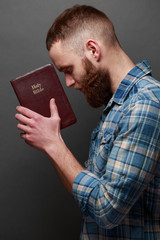 Wall Mural - Handsone man reading and praying over Bible in a dark room over gray texture
