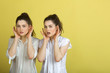 © Alexandr - two beautiful young girl sisters twins in white blouses on a yellow background with expression on their faces