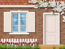 The Facade Of A Country House In The Spring. Brick Wall With Window And Door. In The Front Garden Grow Red Tulips.
