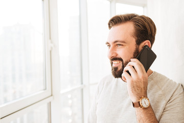 Sticker - Closeup portrait of cheerful guy with beard and mustache looking through window, while having pleasant mobile call