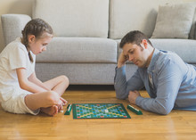 Little Girl And Her Father Playing Scrabble Board Game.