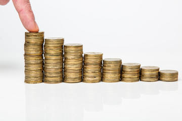 Hand pressing yellow coins in stacks of yellow coins in a row on a white background