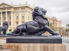 Statue Of A Lion On The Base Of The Pedestal Of The Columbus Monument At The Lower End Of La Rambla, Barcelona, Spain