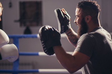 girl training on boxing mitts held by master boxer