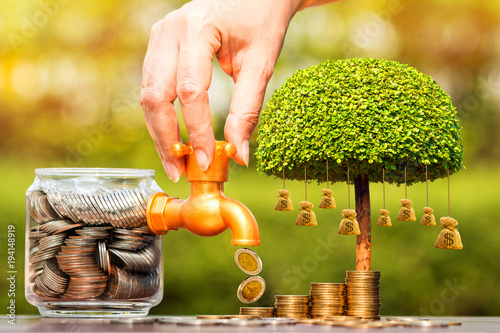 Fotografía Woman's hand open a faucet of jar and gold coin drop for invest benefit growing and tree of money bag put on the wood in the public park, for business financial investment and fund concept