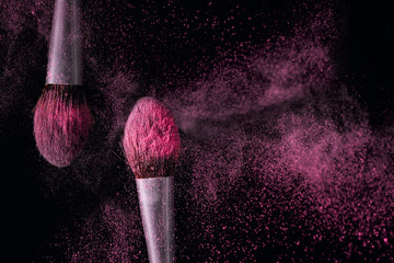 Two brushes for makeup with pink make-up shadows in motion on a dark background.