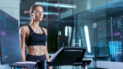 Wall Mural - beautiful woman athlete wearing sports bra with electrodes connected to her, walks on a treadmill in
