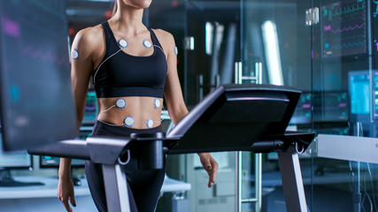 Wall Mural - beautiful woman athlete with electrodes attached to her, running on a treadmill in a sports science 