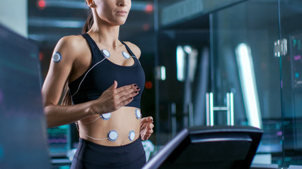 Wall Mural - beautiful woman athlete runs on a treadmill with electrodes attached to her body, female physician u