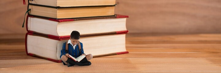 Wall Mural - Boy reading on the floor next to a pile of books