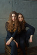 © Alexandr - portrait of two beautiful young girls of twin sisters with flowing hair against the gray wall in the interior