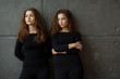 © Alexandr - portrait of two beautiful young girls of twin sisters with flowing hair against the gray wall in the interior