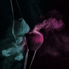 Makeup concept with a single red makeup brush shaking and applying green powder. Colorful dust explosion, closeup. Isolated on black background