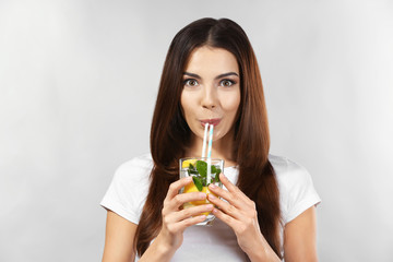 Sticker - Beautiful young woman drinking lemonade on grey background