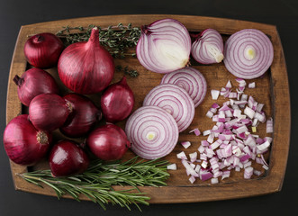 Canvas Print - Cut and whole red onions with herbs on black background