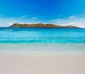 Minimalistic picture. Soft wave of blue ocean on sandy beach with Island in the Background.