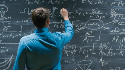 Wall Mural - Mathematician Approaches Big Blackboard and Finishes writing Formula, Turns Around and Smiles on Camera. 