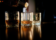 Man Pours Whisky In The Glasses Standing Before A Wooden Table