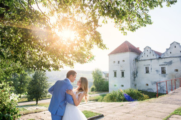Wall Mural - Groom holds bride tender posing with her before an old castle in a sunny summer day