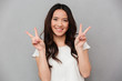 © Drobot Dean - Portrait of cute asian girl 20s in casual t-shirt and jeans smiling and showing peace sign with both hands, isolated over gray background