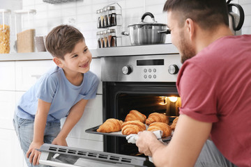 Little boy watching his father bake croissants in oven indoors