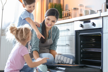 Poster - Woman treating children to cookies indoors. Fresh from oven