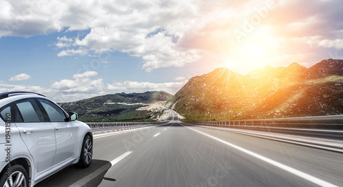 A white car rushing along a high-speed highway in the sun.