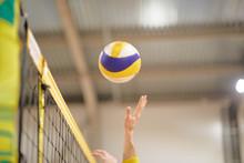 The Volleyball Player's Hand In The Covered Gym Fights The Ball In Front Of The Net,