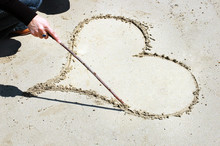 Girl Draws A Heart With A Stick On The Sand