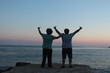 © evmez - two young men thumb up near sea, background is sunset