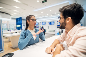 Wall Mural - Beautiful young brunette talking with employe in the tech store.