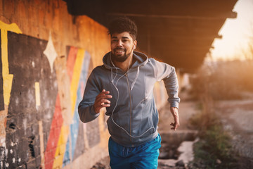 portrait of active motivated afro-american young attractive athletic man with earphones running insi