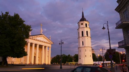 Poster - Vilnius, Lithuania. Illuminated Cathedral of Vilnius, Lithuania and Bell Tower at night. Time-lapse of dark blue cloudy sky, car traffic trails at the foreground