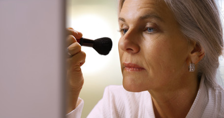 Attractive mid aged woman applying blush makeup