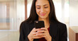 © Mark Adams - A Latina office professional texts on her mobile phone at work. A Hispanic office worker uses her smart phone in her office