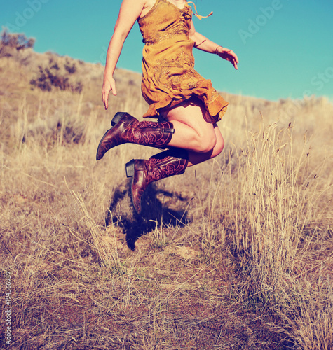 Fotografie, Obraz pretty woman in a skirt jumping up in cowboy boots in a wheat field on a hot sum