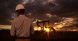 © Mark Adams - Engineer wearing hard hat helmet checking oil derrick field. Sunset as man looks at oil pump rig