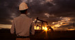 © Mark Adams - Engineer wearing hard hat helmet checking oil derrick field. Sunset as man looks at oil pump rig