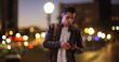© Mark Adams - Millennial Hispanic man standing on city bridge at night looking at smartphone. Latino guy on urban street in the evening using cell phone