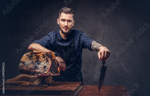 Fotografie, Obraz Professional butcher holds a knife standing with raw smoked meat