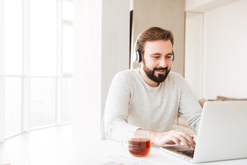 Sticker - Photo of content man with short brown hair and beard listening to music via wireless headphones, while working on notebook