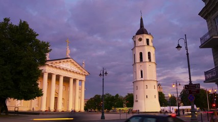 Poster - Vilnius, Lithuania. Illuminated Cathedral of Vilnius, Lithuania and Bell Tower at night. Time-lapse of dark blue cloudy sky, car traffic trails at the foreground. Zoom in