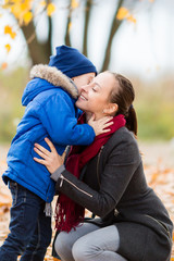 Young Mother and son in autumn park. happy family: mother and child boy play cuddling on autumn walk in nature outdoors