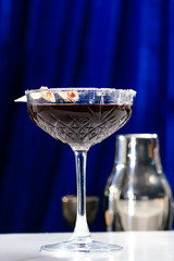 Wall Mural - Martini glass with dark alcoholic cocktail at the bar counter on blue background