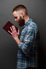 Wall Mural - Handsone man reading and praying over Bible in a dark room over gray texture