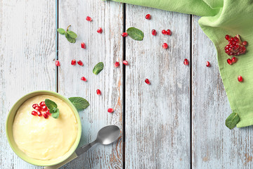 Wall Mural - Tasty vanilla pudding with pomegranate seeds in bowl on wooden background