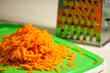 Carrots grated on a metal grater on a cutting board of green color