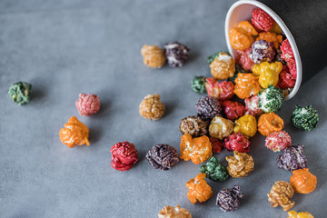 Multicolored popcorn and black paper cup on gray background.